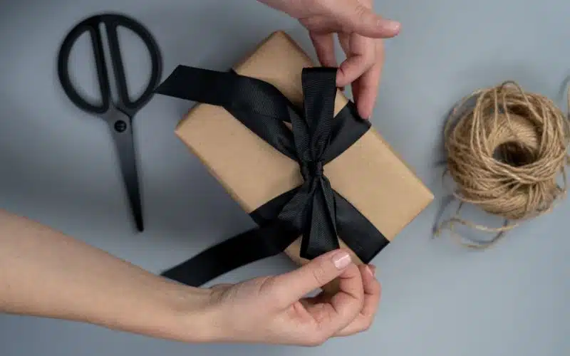 Hands tying a black bow on a box